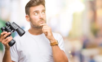 man thinking deeply while holding a pair of binoculars