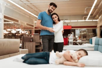 a couple watching a little girl sleeping in a mattress store