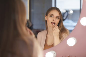 young lady looking at reflecton while applying lip gloss